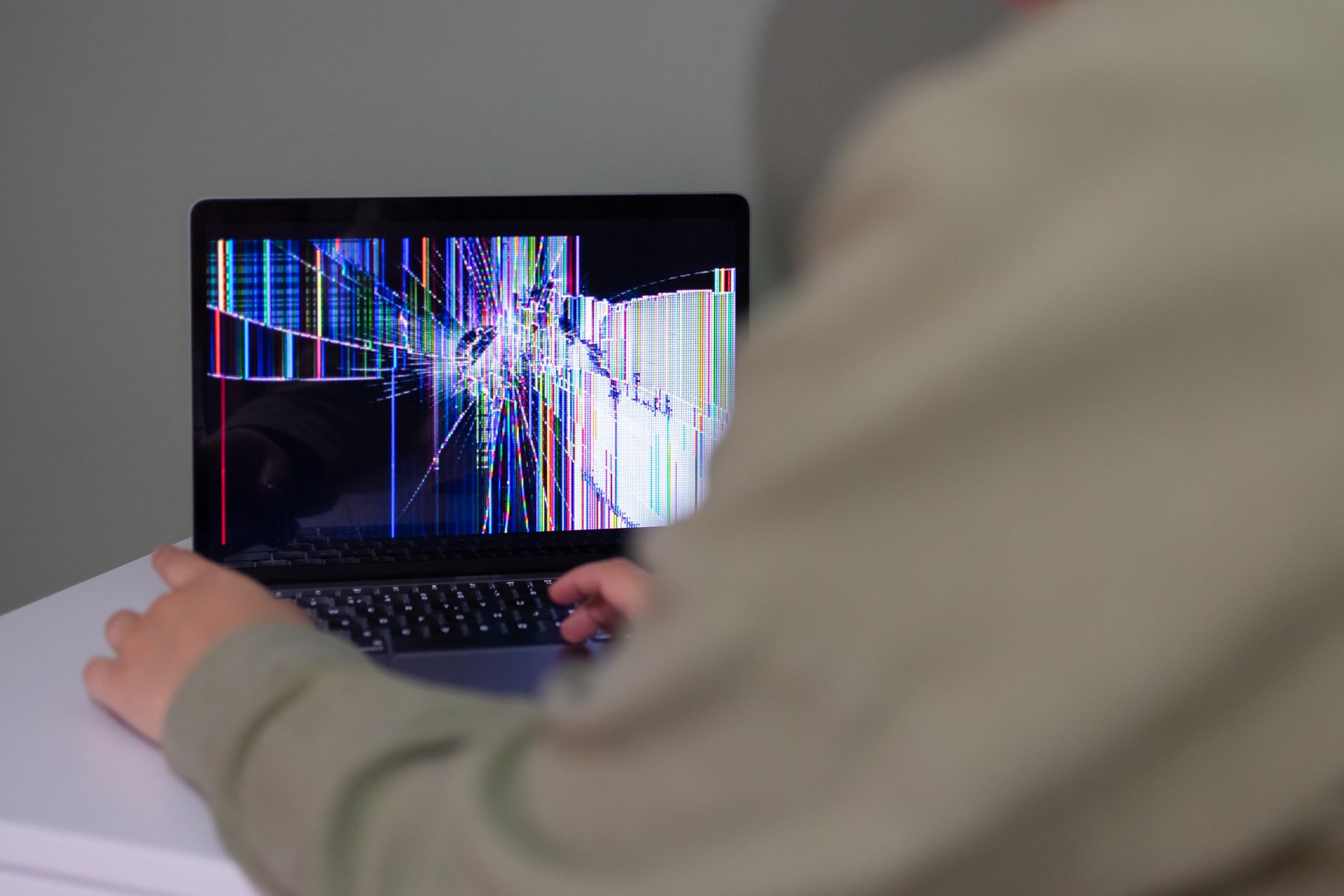 A person interacts with a laptop that has a cracked and distorted screen.
