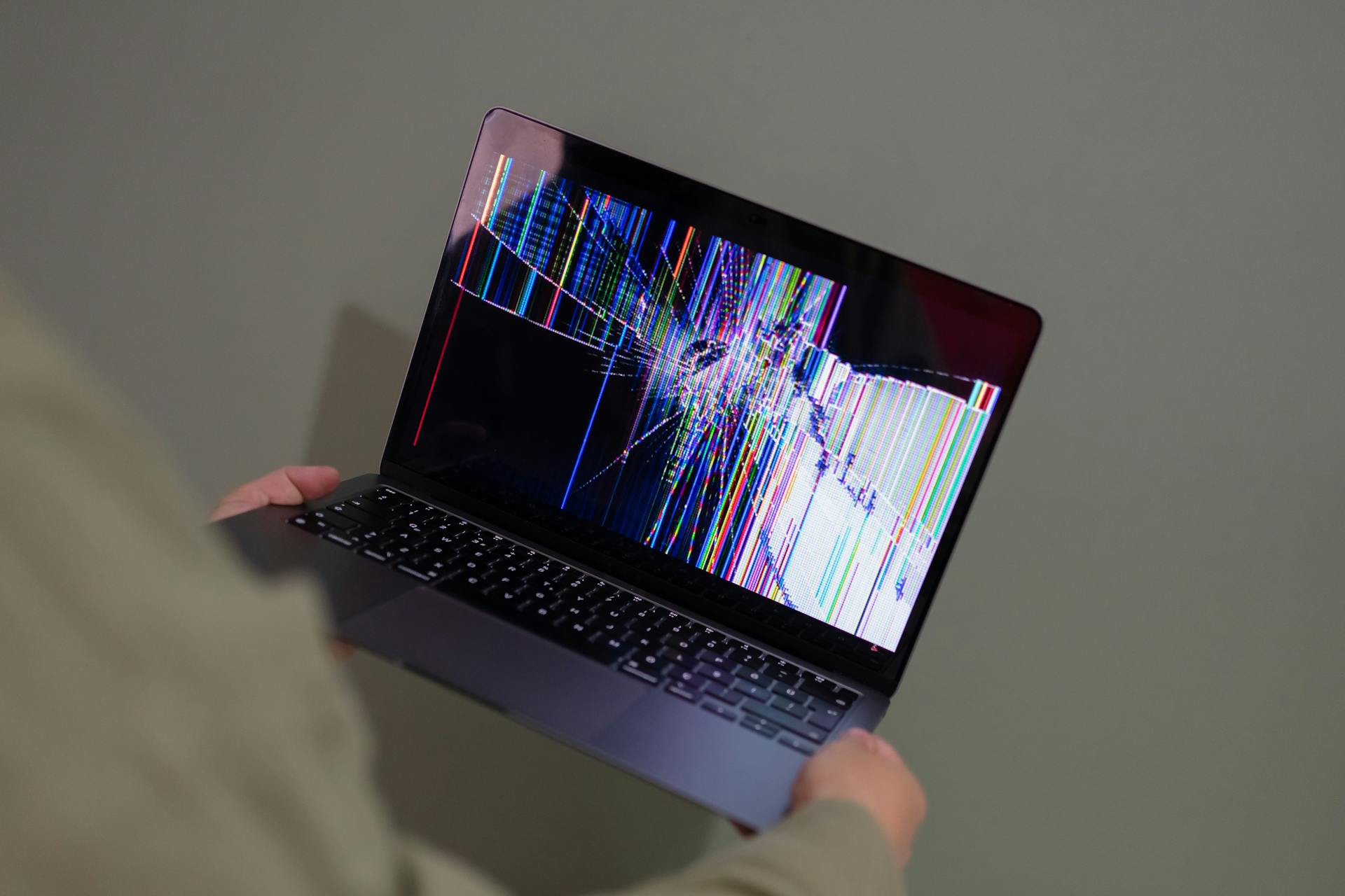 A person holding up a laptop with a broken screen