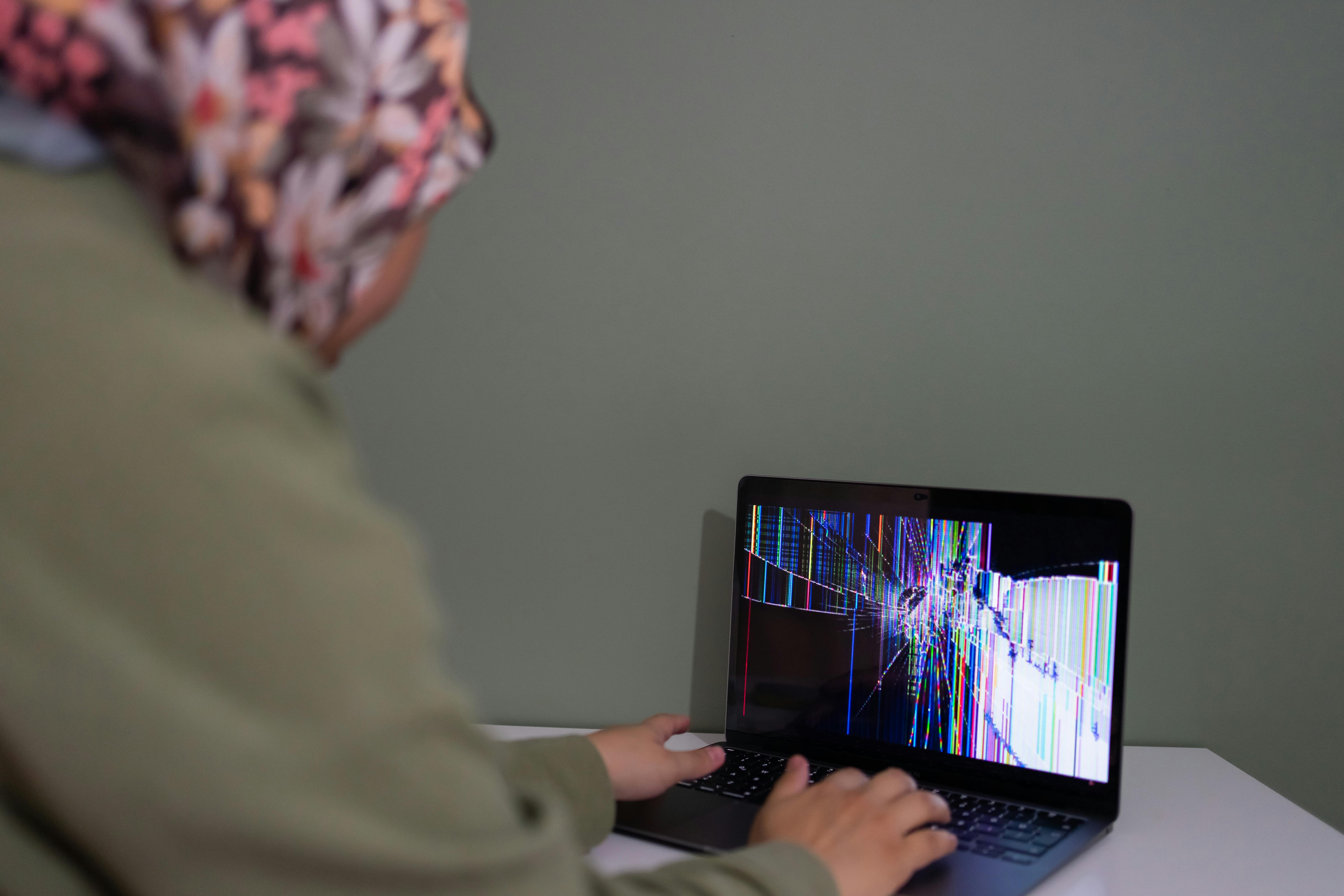 A person interacts with a laptop displaying a colorful cracked screen indoors.