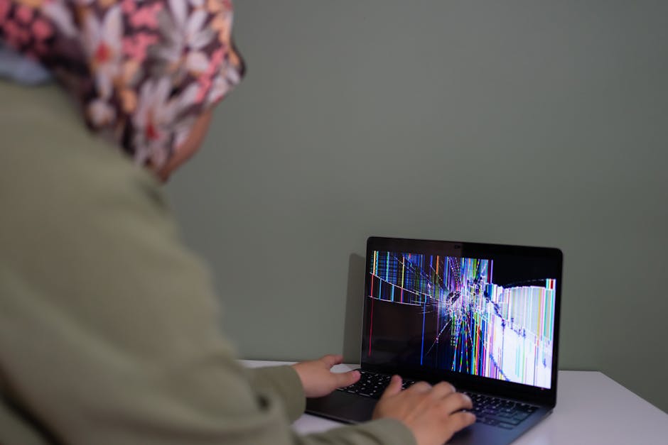 A person interacts with a laptop displaying a colorful cracked screen indoors.
