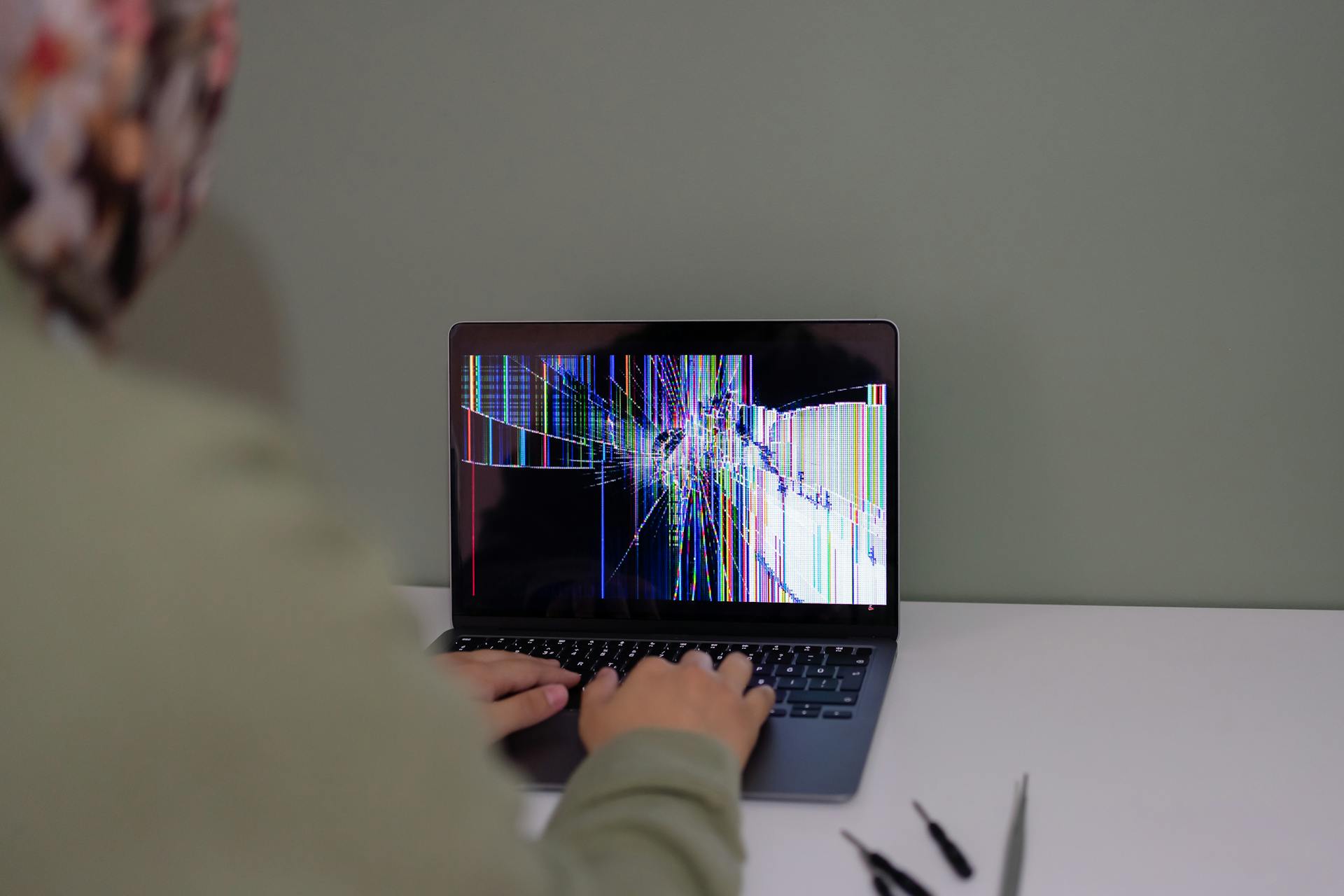 Adult working on a laptop with a cracked screen, indoors setting.