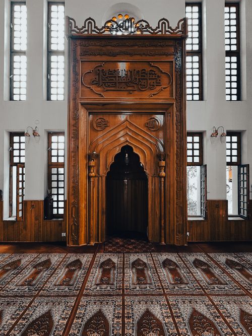 Free Capture of a traditional mosque interior featuring an intricately carved wooden mihrab and elegant windows. Stock Photo