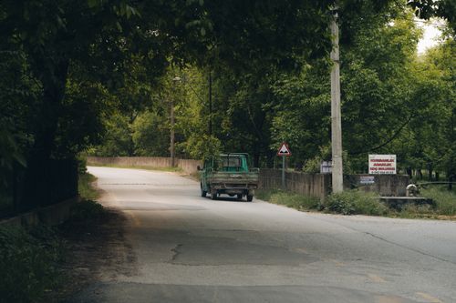 Free A vintage truck travels along a rural road flanked by lush green trees, offering a serene countryside view. Stock Photo