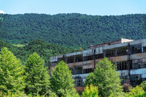 Free Aged industrial building amidst lush green mountains in Gagra, depicting nature reclaiming urban spaces. Stock Photo