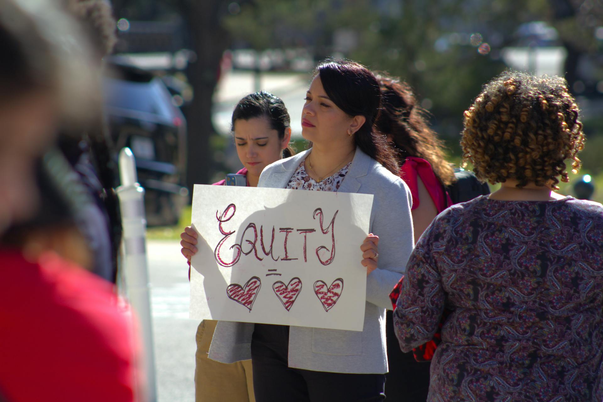 Women marching for equity holding signs in an outdoor protest in Austin, TX.