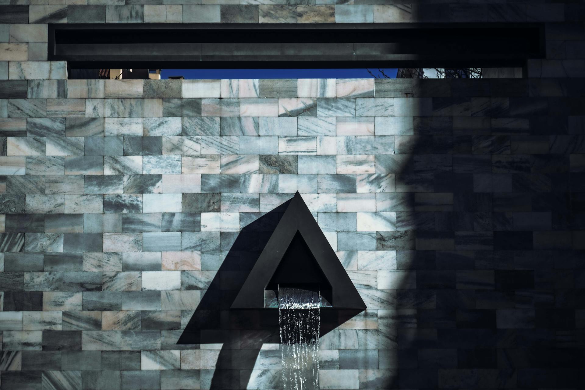 Modern waterfall feature on patterned stone wall with abstract design and triangle shape.