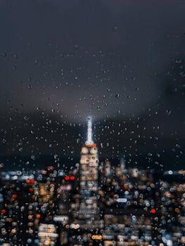 Night view of New York City skyline blurred through a raindrop-covered window.