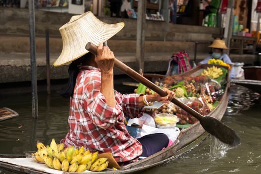Woman paddling boat at a vibrant floating market in Bangkok, Thailand.