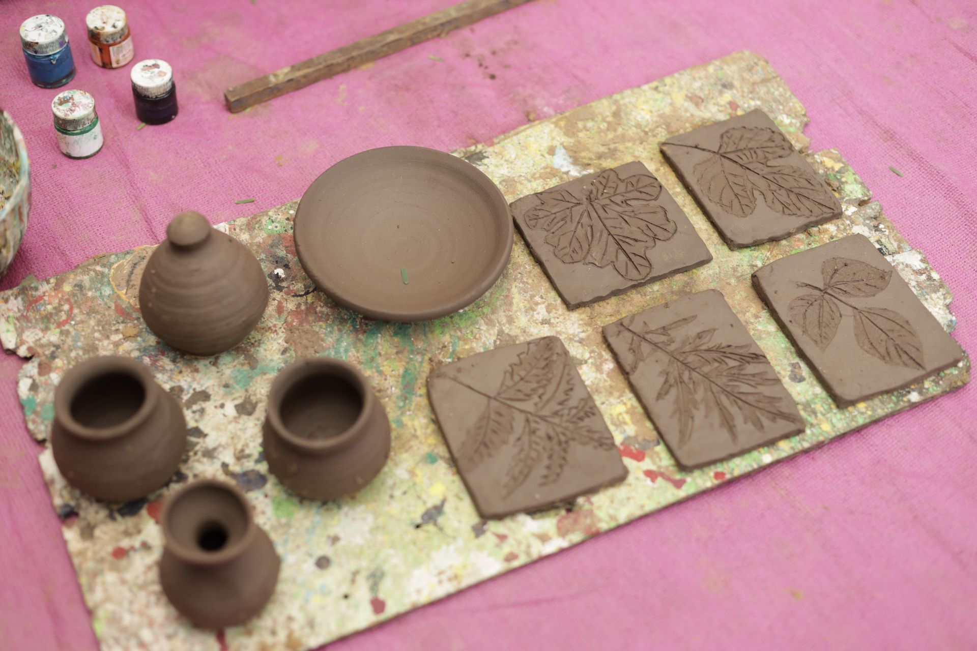 A collection of handcrafted pottery and leaf impression clay tiles on a textured surface.