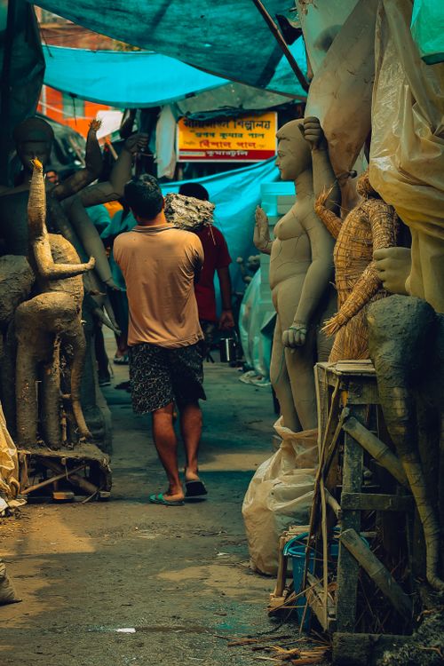 Free A man walking through a market stall filled with clay sculptures, creating a cultural and artistic atmosphere. Stock Photo