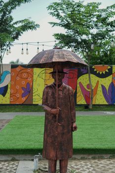 Bronze statue of a man holding an umbrella, set against a colorful mural.