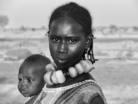 Black and white portrait of a woman with intricate jewelry holding a child in Mali.