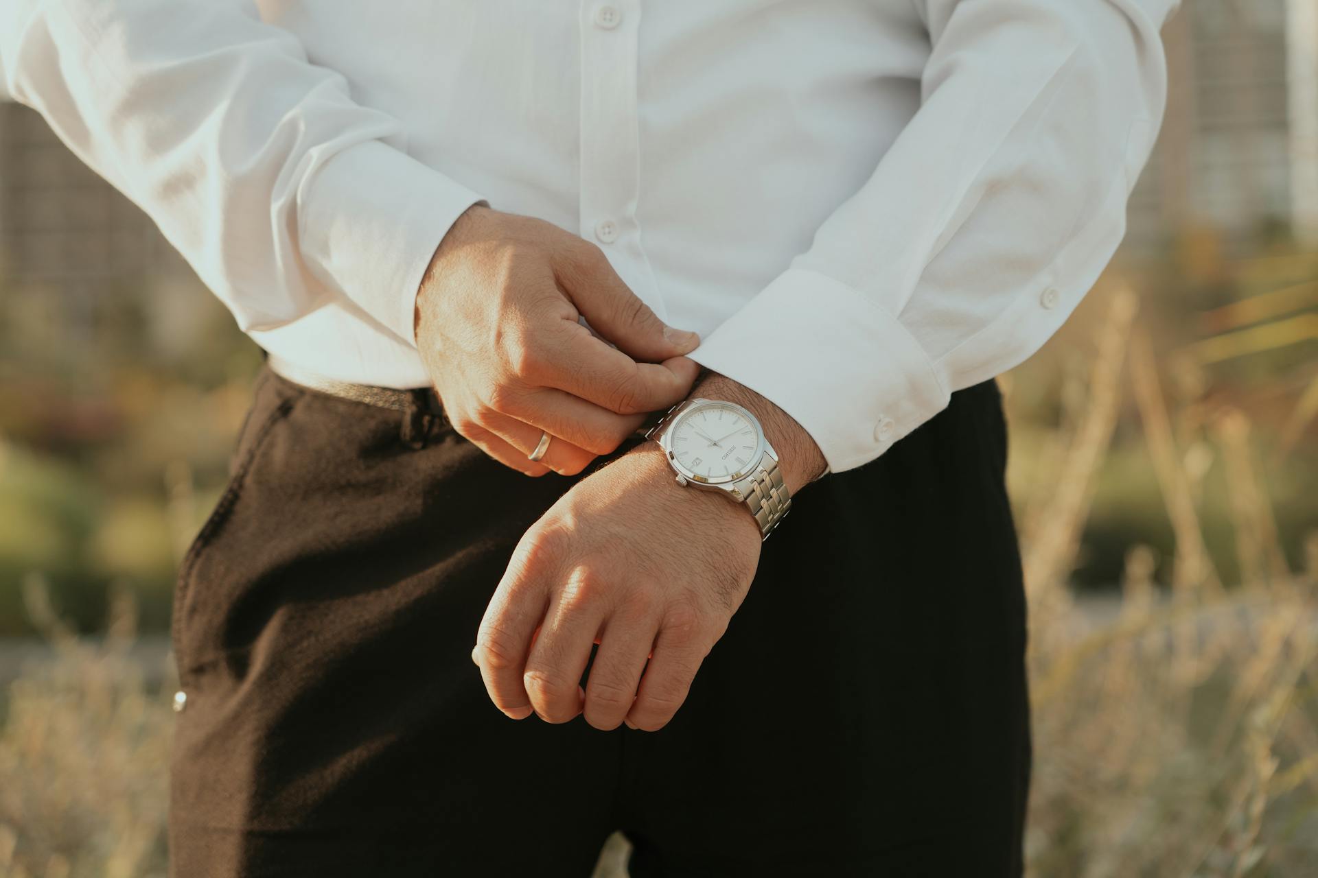 Close-up of a man adjusting a silver wristwatch outdoors in natural light.