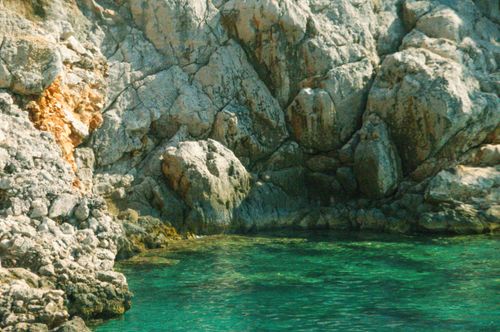 Free A beautiful rocky cliff face meeting a clear turquoise sea, ideal for nature and travel content. Stock Photo