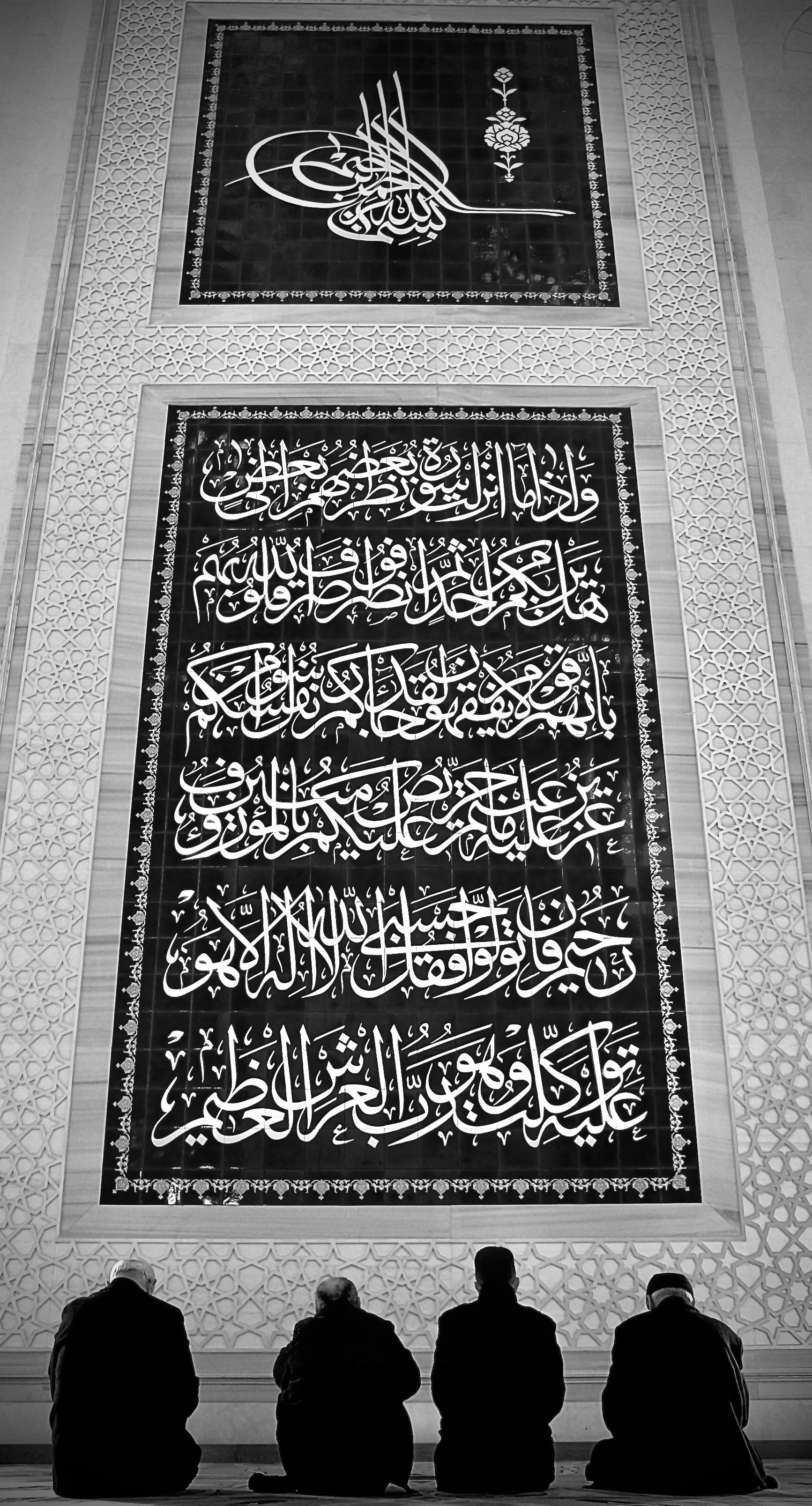 Silhouetted figures praying before Islamic calligraphy in a mosque.