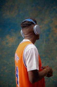 Back view of a man wearing headphones and an orange sports jersey.