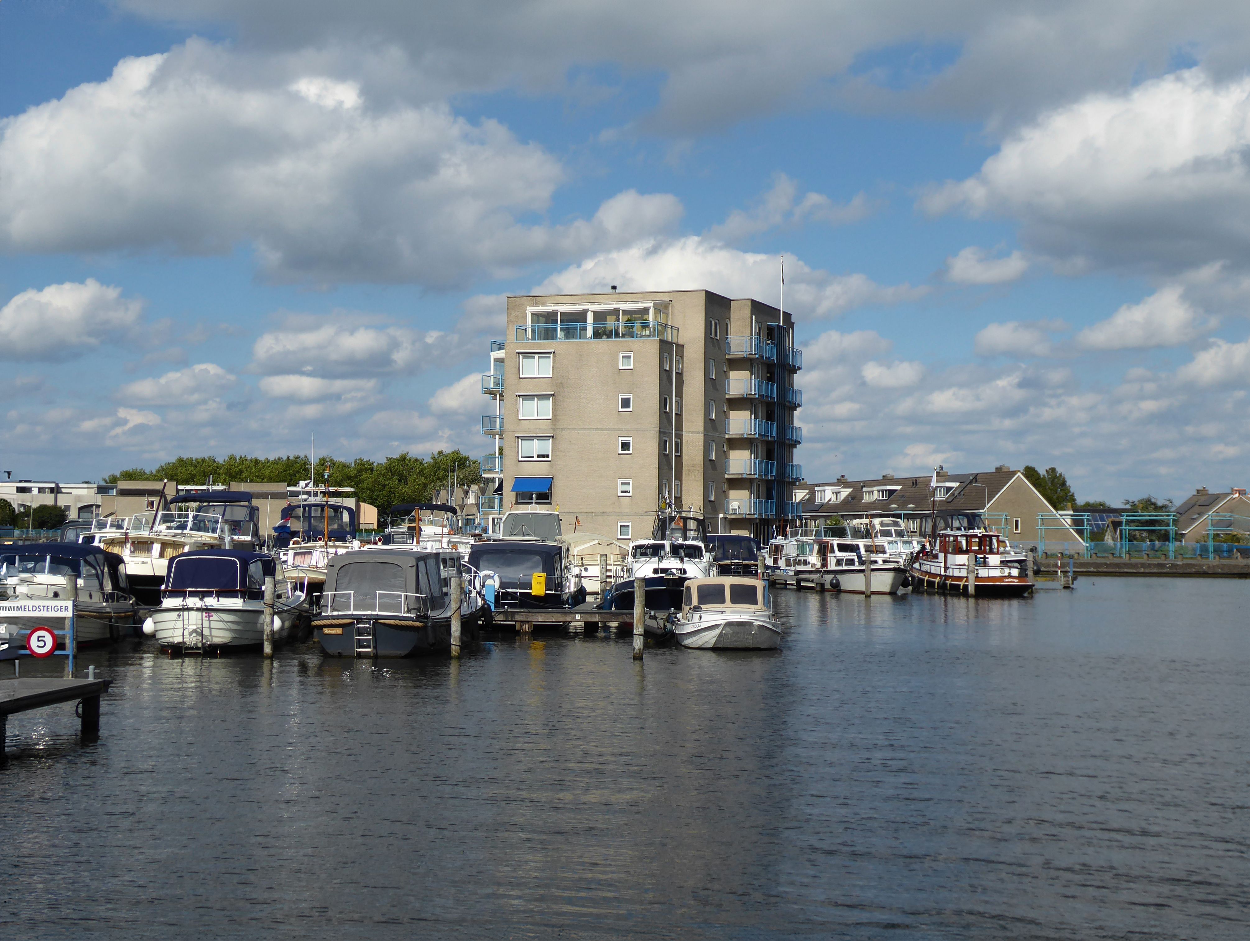 A peaceful marina scene with anchored boats and a modern apartment building under a clear blue sky.