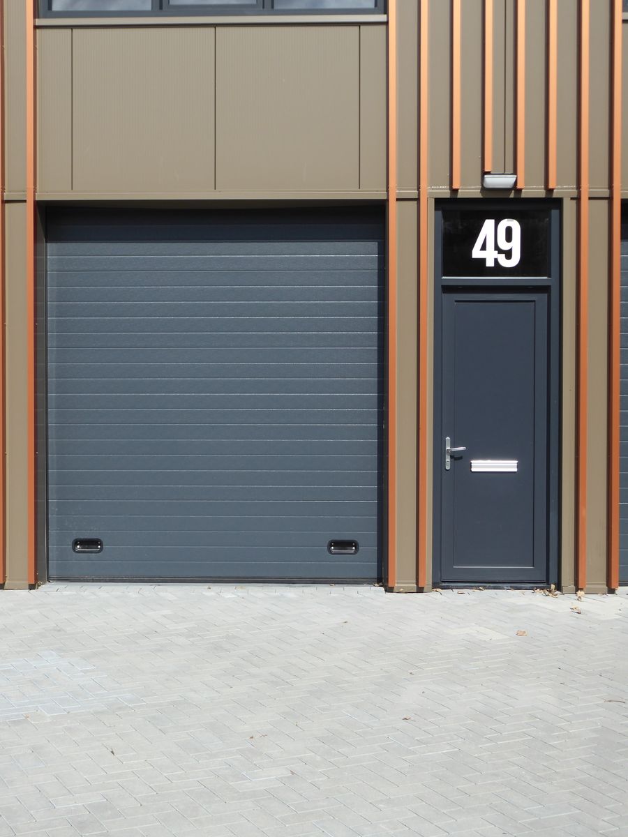 Modern charcoal-gray roll-up garage door with matching entry door, house number 49