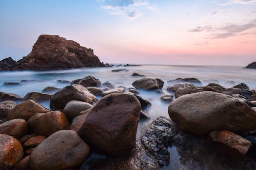 Beautiful sunset at rocky seashore in Acapulco, Mexico with a calm ocean and pastel sky.