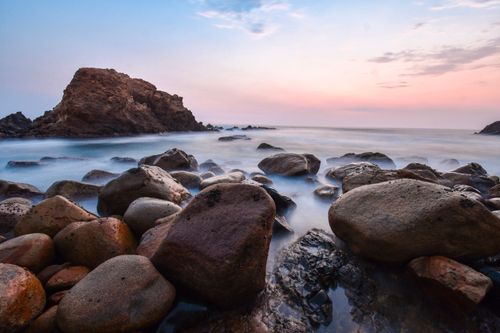 Free Beautiful sunset at rocky seashore in Acapulco, Mexico with a calm ocean and pastel sky. Stock Photo