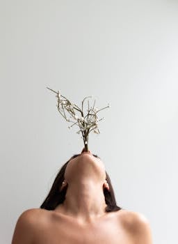 Minimalist portrait of a nude woman holding a branch against a white background, creating an artistic pose.