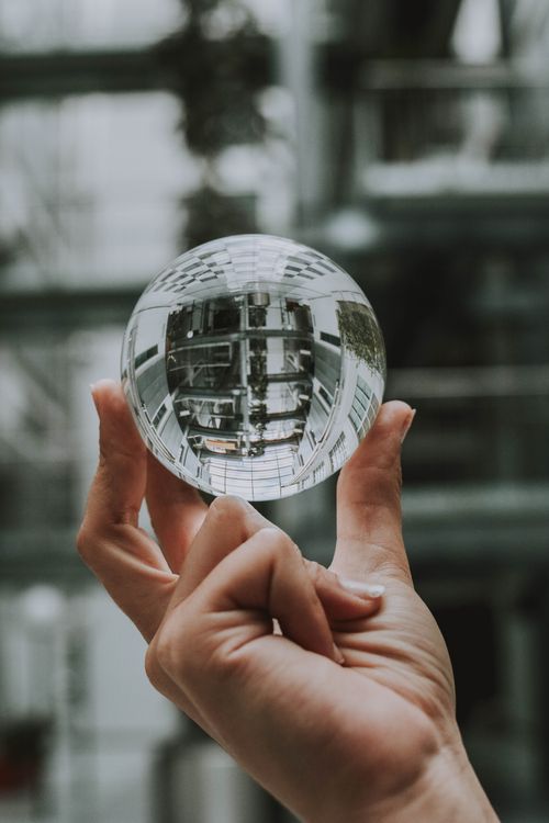 Free Close-up of a hand holding a glass sphere reflecting an indoor setting with a blurred background. Stock Photo