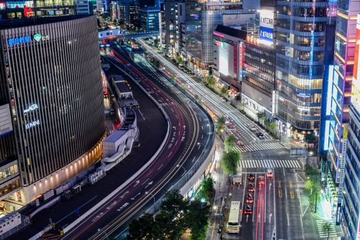 A long exposure shot of Tokyo's busy urban landscape with illuminated skyscrapers and bustling traffic at night.
