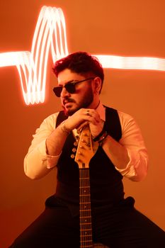 Man in sunglasses holding guitar with neon heartbeat design background.