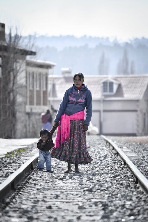 Woman Holding Toddler While Walking on Railway