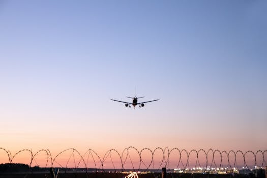 A serene shot of an airplane landing over a barbed wire fence at sunset in Mārupe, Latvia.