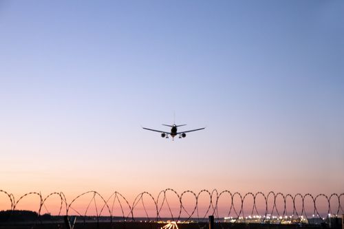 Free A serene shot of an airplane landing over a barbed wire fence at sunset in Mārupe, Latvia. Stock Photo