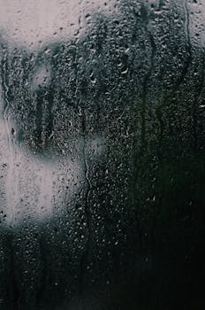 A dark and textured close-up of rain on a glass surface, capturing reflections and moodiness.