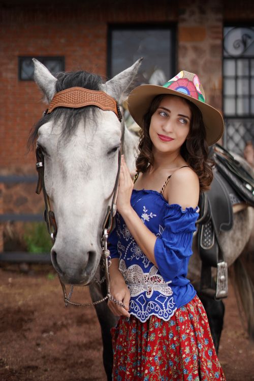 Free A smiling woman in vibrant attire stands beside a beautiful gray horse outdoors. Stock Photo