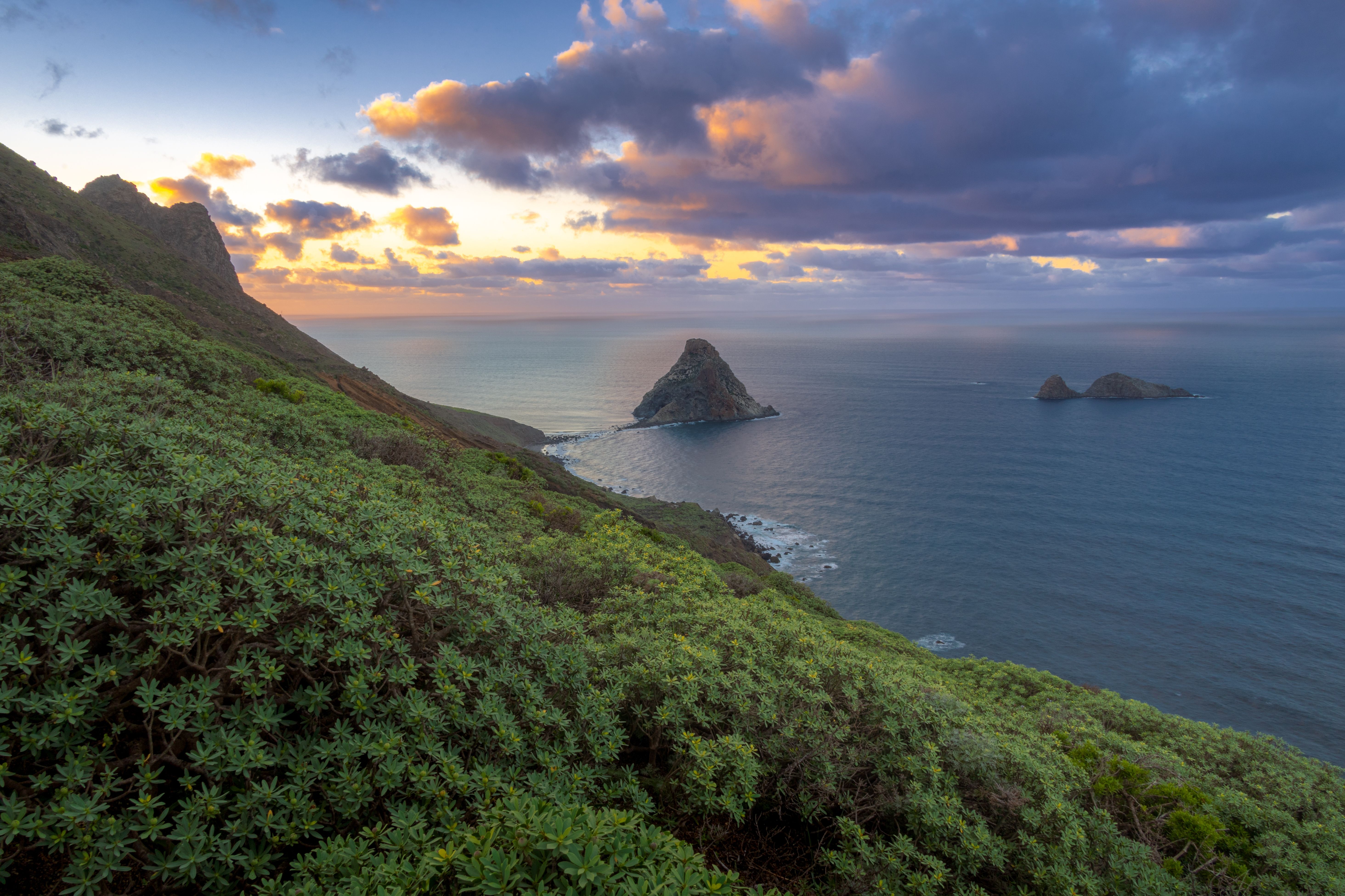 A sunset over the ocean and green hills · Free Stock Photo