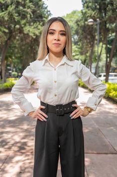 A confident woman poses outdoors in a park in Ciudad de México, wearing business casual attire.