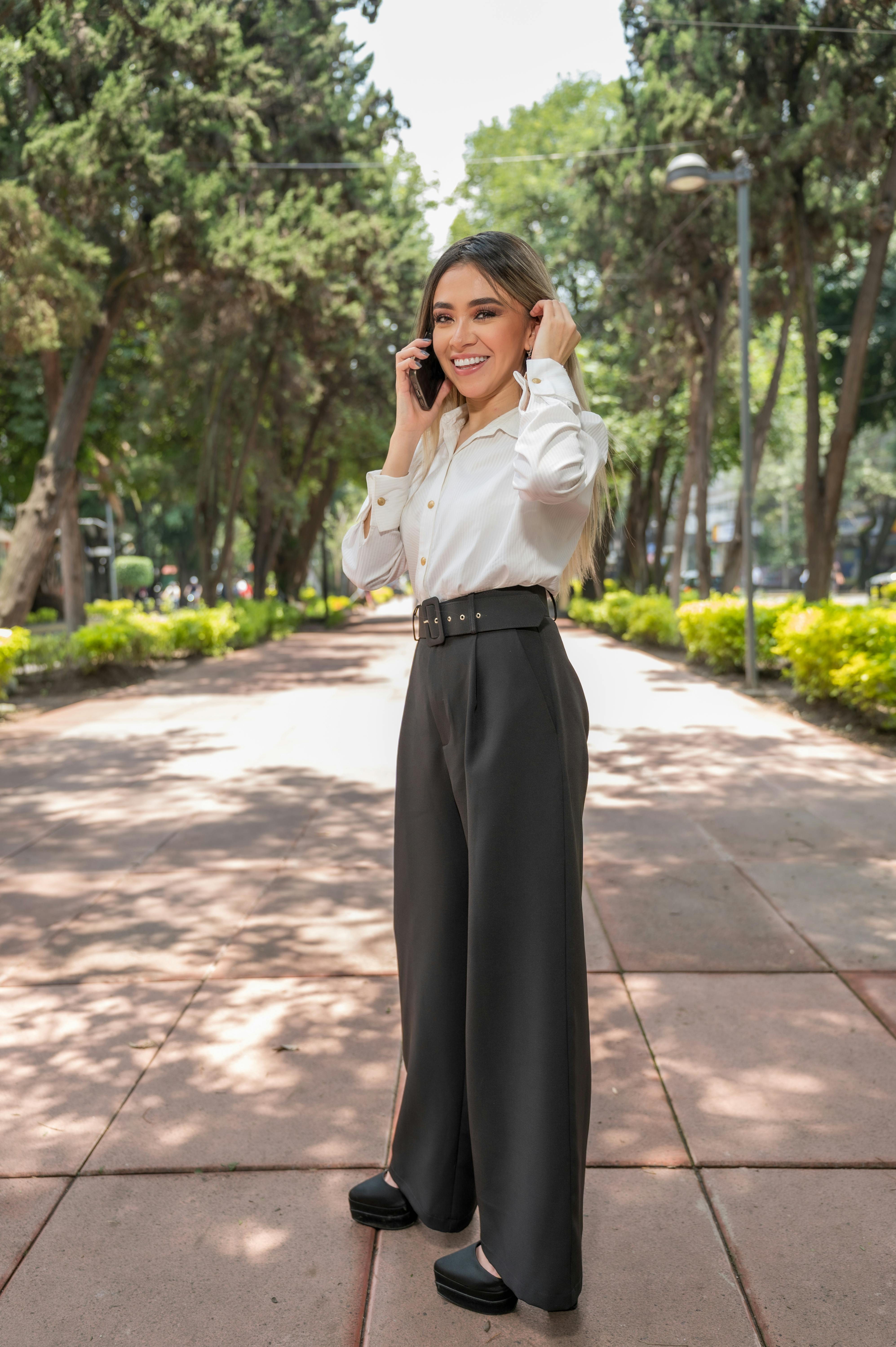 Elegant woman in business attire talking on the phone in a serene park setting in Ciudad de México.