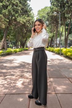 Elegant woman in business attire talking on the phone in a serene park setting in Ciudad de México.