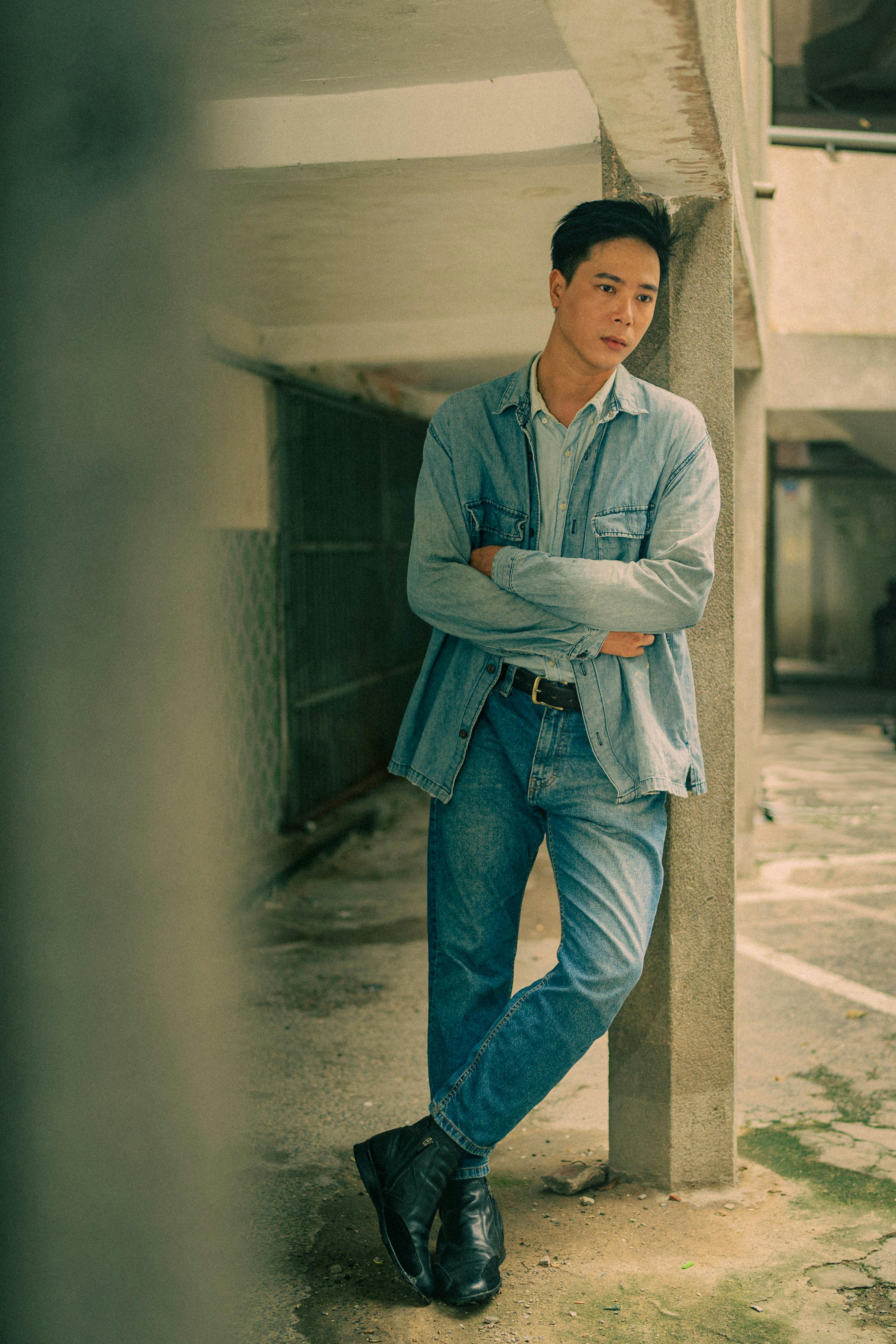 A fashionable man leans against a pillar in a casual denim ensemble.