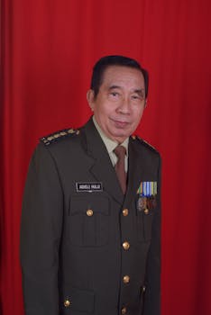 Portrait of senior military officer in green uniform with medals against red backdrop.