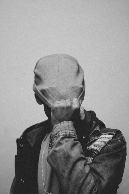 Black and white portrait of a person covering their face with a beanie in a moody atmosphere.