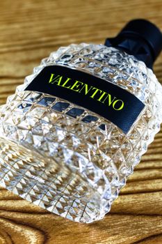A close-up shot of a Valentino-branded crystal glass perfume bottle on a wooden surface.