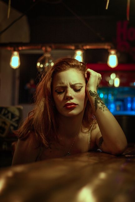 Relaxed woman with red hair leaning on a rustic bar counter indoors, Rio de Janeiro.