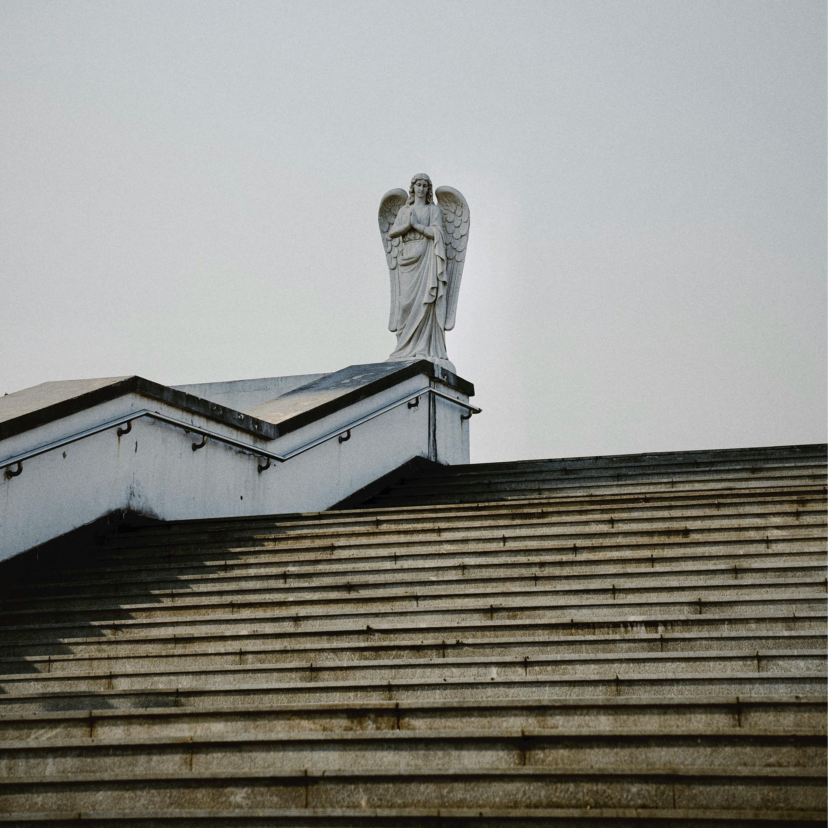 A peaceful angel statue stands atop a rooftop staircase, offering a glimpse of tranquility against the sky.