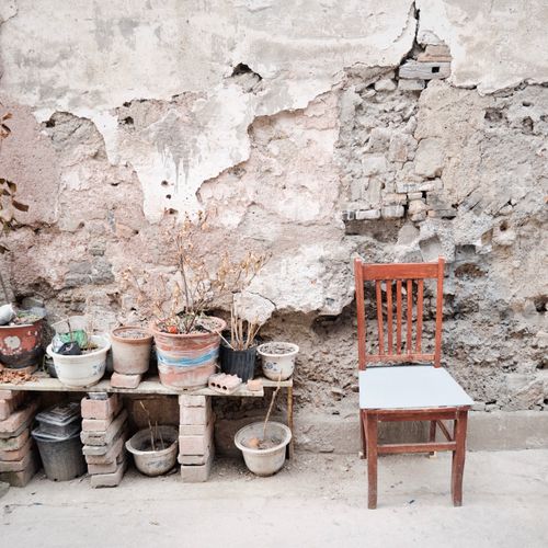 Free A rustic outdoor scene featuring a chair and potted plants against a weathered wall. Stock Photo