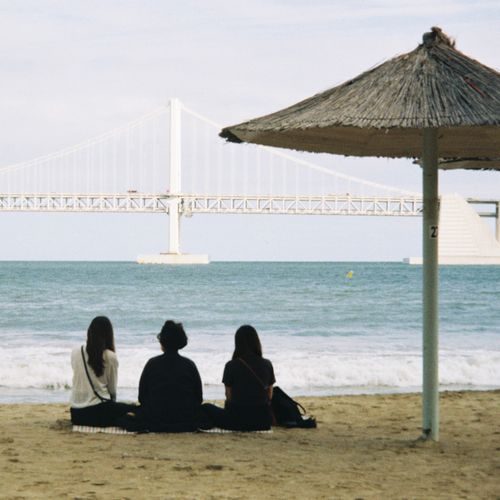 Free Three people enjoying a peaceful moment on a beach facing the iconic Gwangan Bridge. Stock Photo