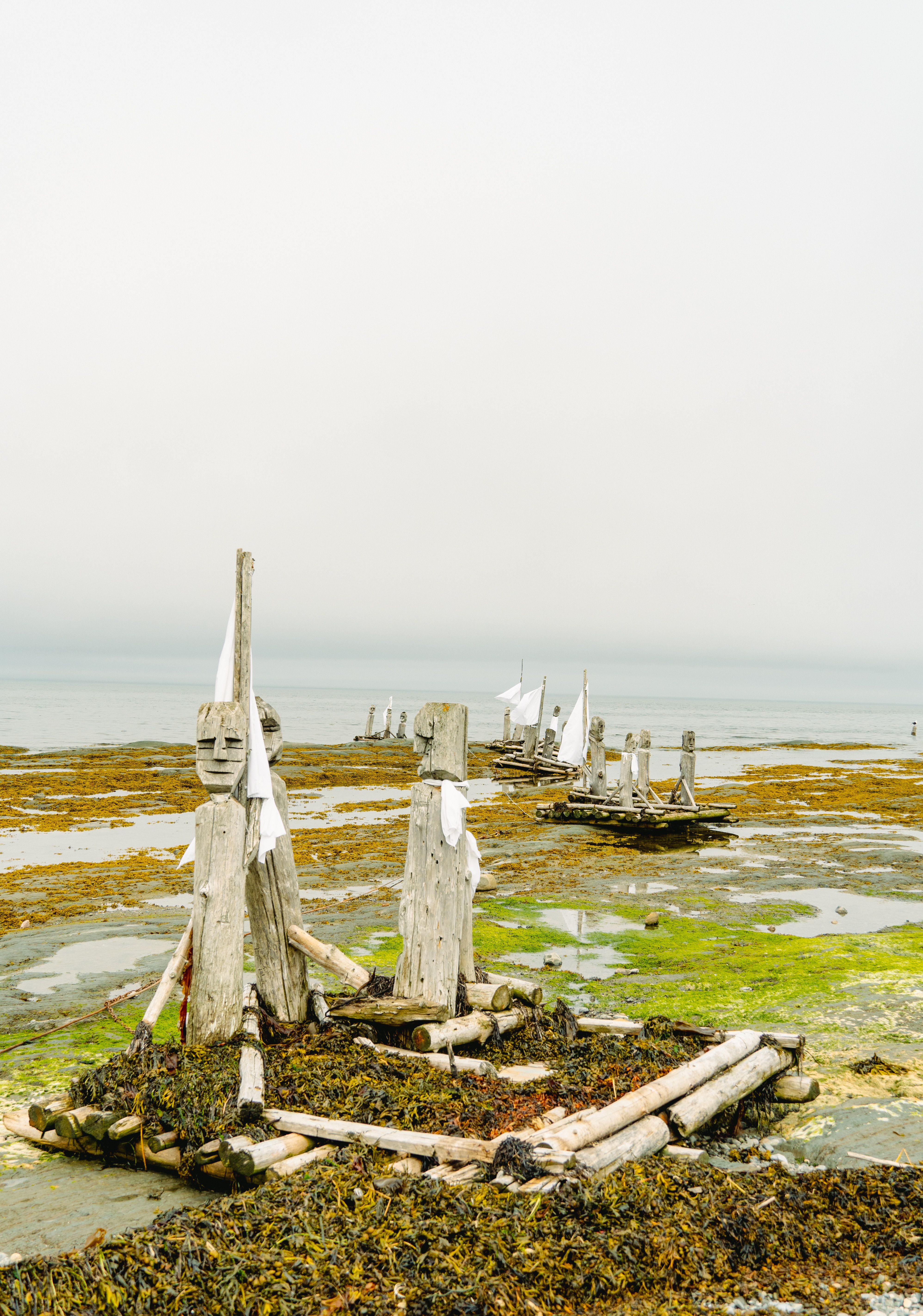 Artistic wooden sculptures on Sainte-Flavie beach, capturing creativity and nature's beauty.