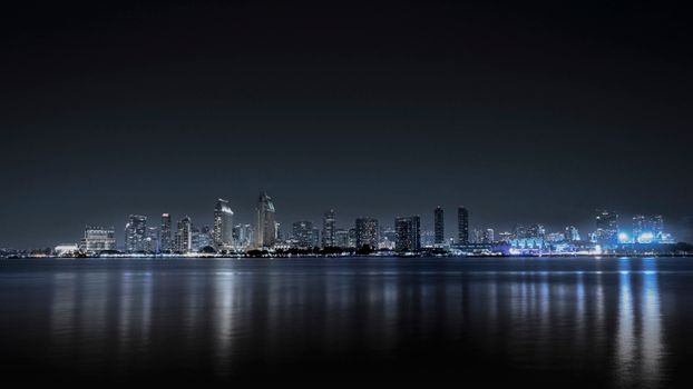 San Diego city skyline lit up at night, reflected on calm waters.