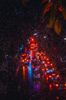 Raindrops on a window with blurred night city lights of Bangkok, capturing the vibrant nightlife.