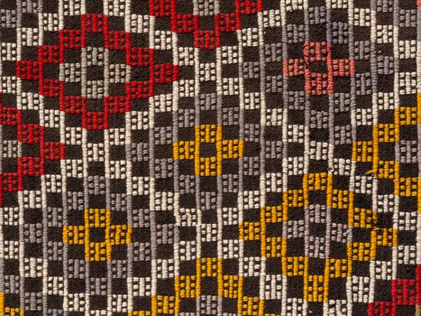 Close-up of a vibrant woven textile with intricate geometric patterns in red, yellow, and gray.