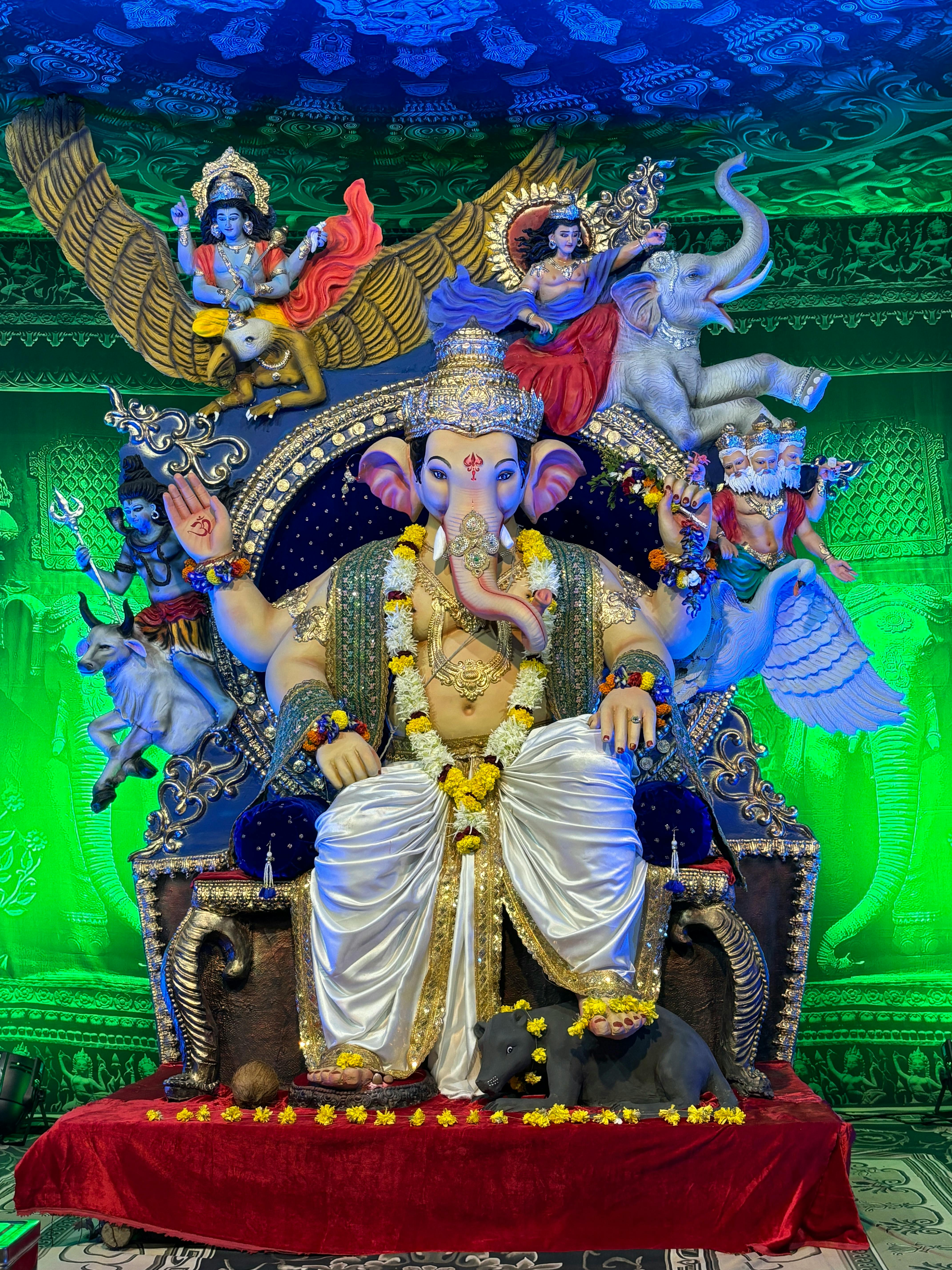 Vibrant Ganesh statue adorned with flowers in a temple setting, surrounded by intricate decorations.